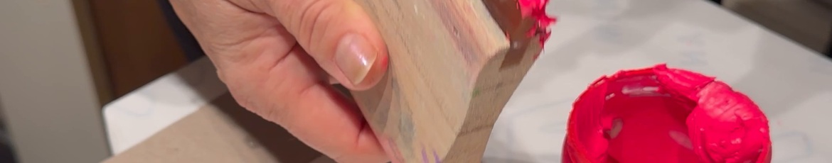 Hand mit Holzrakel und neonpinker Siebdruckfarbe neben dem offenen Farbtopf