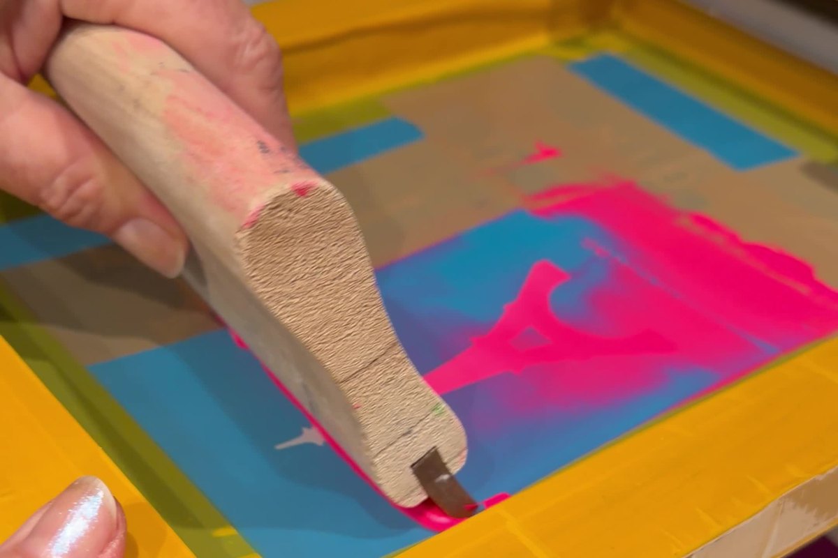 Hand zieht die Farbe mit dem Rakel durch das Sieb
