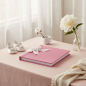 Preview: Trixi Gronau SABRINA photo album rose pink stingray-textured (beluga) leather with white satin ribbon bow on blush pink linen with baby shoes, white peony and cream knit blanket in airy nursery corner