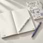 Preview: Caran d'Ache Toile de Jouy White Blue writing instruments with Geneva illustrations on an open notebook
