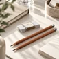 Preview: Graf von Faber-Castell Schreibset mit weißem Radiergummi, versilberter Manschette und zwei Zedernholzbleistiften auf hellem Schreibtisch, KI-gestaltete Szene