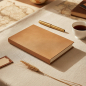 Preview: Trixi Gronau MAZZI A5 notebook Kanuba camel on linen tablecloth with brass pen, black tea and leather travel tag