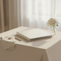 Preview: Trixi Gronau ISA photo album white iguana-embossed Skivertex on linen tablecloth with white peony, gold wedding band and gold pen in airy bridal suite