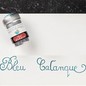 Preview: Jacques Herbin Bleu Calanque Aluminiumdose neben türkisblauer Kalligrafie auf weißem Papier