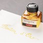 Preview: Jacques Herbin Bouton d’Or Tintenflakon neben goldgelbem Kalligrafie-Schriftzug auf weißem Papier