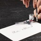 Preview: Tintenpatrone Perle Noire wird in einen Füllhalter eingesetzt, daneben die geöffnete Aluminiumdose