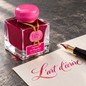 Preview: Jacques Herbin Fuchsia de Magellan Tinte neben cremefarbenem Papier mit pinkfarbener Kalligrafie und goldenen Schimmerreflexen