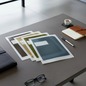 Preview: Julifoli MONO BUSINESS document sleeves, fanned out on a modern dark-grey desk. Five transparent A4 sleeves in muted professional tones (olive, mustard gold, dark green, petrol blue, anthracite) with leather portfolio, cognac notebook and an espresso. Ref