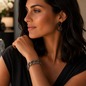Preview: KMO Gliederarmband CRISSY schwarz-gold, worn on the wrist of an elegant woman with long dark hair, hand at the chin, soft sideways gaze. Wide cuban link bracelet with dark hammered silver finish and fine pavé sparkle, paired with matching black-gold state