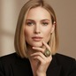 Preview: KMO Ring MONA LISA Statement oliv-gruen am Mittelfinger einer eleganten Frau mit schulterlangem, naturblondem Haar, Hand sanft an Kinn und Hals gelegt. Grosser runder Dome-Ring mit dicht gesetztem Silber-Pavé auf der oberen Haelfte und warm oliv-goldenem 