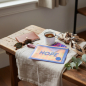 Preview: Lightree Pouch L kompakte kleine Zip-Tasche in HOPE BLUE recycelter Stoff mit rundem Logo-Patch, liegend auf hellem Leinentuch auf Holzbank mit Lederpasshülle, Emaillebecher Kräutertee, runder Vintage-Sonnenbrille, gefaltetem Sandfarbenem Foulard und Euka
