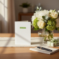 Preview: Trixi Gronau congratulations card BEST WISHES, B6 portrait in white pearlescent paper with a small fresh-green rectangular label and the words best wishes in white lowercase sans-serif, centered in the upper third. On a warm light-oak desk with cream line