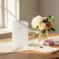 Preview: Trixi Gronau congratulations card STRAIGHT FROM MY HEART, B6 portrait in white pearlescent paper with a small magenta heart in a laurel wreath and delicate grey script. On a warm light-oak desk with cream linen runner, beside a bouquet of white peonies, s