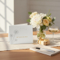 Preview: Trixi Gronau congratulations card WÜNSCH DIR WAS, B6 landscape in white pearlescent paper with three delicate grey dandelions on the left and WUENSCH DIR WAS! in mustard-yellow sans-serif on the right. On a warm light-oak desk with cream linen runner, bes
