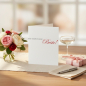 Preview: Trixi Gronau greeting card DU BIST DIE BESTE, B6 portrait in white pearlescent paper with grey serif type and large red calligraphic script Beste!. On a warm light-oak desk with cream linen runner, beside soft pink garden roses, white peonies, eucalyptus 