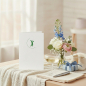 Preview: Trixi Gronau GOLF greeting card, B6 portrait in white paper with a small graphic golfer mid-swing in fine dark-green lines, framed by a delicate green arc, centered on the upper third. On a light oak desk with a small vase of white peonies, eucalyptus and