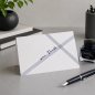 Preview: Trixi Gronau ZUR TAUFE Glueckwunschkarte, B6 Hochformat mit feinen marineblauen diagonalen Linien die sich kreuzen, in der Mitte in fliessender marineblauer Handschrift zur Taufe. Aufgestellt auf weicher cremefarbener Strickdecke mit kleinem Strauss weiss