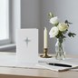 Preview: Trixi Gronau Trauerkarte KREUZ DOTTED, B6 Hochformat in reinem Weiss mit feinem dunkelgrauen Kreuz aus Punkte-Raster (Halbton-Muster) in der oberen Mitte. Auf hellem Schreibtisch mit cremefarbenem Leinen-Laeufer, daneben kleines stilles Bouquet aus weisse