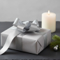 Preview: Vivant Geschenkband METALLIC SHINE silber (38 mm) als grosse glaenzende Schleife auf Geschenk in hellgrauem Papier, mit Tannenzweig und Silberkugel auf dunklem Schiefer. Moderne Weihnachts-Eleganz. Trixi Gronau Concept Store, Hamburg-Lokstedt.