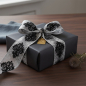 Preview: Vivant Geschenkband ORNAMENTAL schwarz und grau (60 mm) mit kunstvollem Jacquard-Muster als breite Schleife auf Geschenk in dunklem Anthrazitpapier, mit Distel und Messing-Anhaenger auf Walnussholz. Edle maennliche Verpackungs-Stimmung. Trixi Gronau Conce