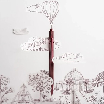 Caran d'Ache 849 Toile de Jouy Burgundy in front of a paper-cut scene from the Geneva illustration