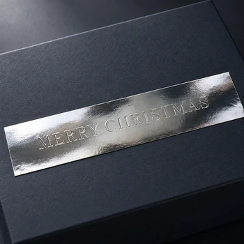 Preview: Silberfarbener Embacollage SILVIO MERRY CHRISTMAS Aufkleber mit Blindprägung auf einer dunklen Geschenkbox, elegante Weihnachtsverpackung