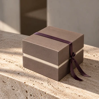 Preview: Embacollage MOKKA Geschenkbox mit Rahmenprägung und auberginefarbenem Geschenkband auf hellem Natursteintisch, elegante Geschenkverpackung