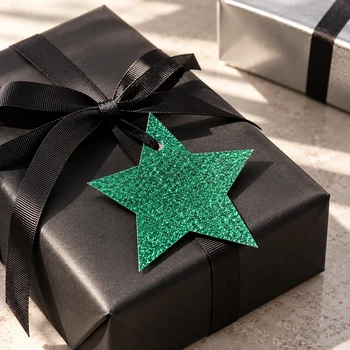 Preview: Grüner Embacollage Glitzerstern als Geschenkanhänger an schwarzer Geschenkverpackung mit schwarzer Ripsbandschleife, inszenierte Lifestyle-Aufnahme