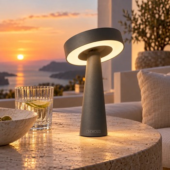 Preview: Anthrazitfarbene NEWDES TIP von Sompex mit leuchtendem LED-Ring auf einem runden Natursteintisch bei Sonnenuntergang, KI-gestaltete Umgebung