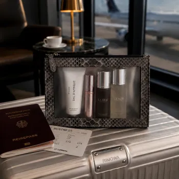 Preview: Janice Boarding Bag mit grauem Schlangenleder und Kosmetikprodukten auf einem Koffer in einer Flughafen Lounge.