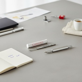 Preview: Caran d'Ache Goliath ballpoint refill in its original white-and-red packaging next to a deconstructed 849 ballpoint showing where the new refill fits, with handwritten test strokes in blue. Premium writing essentials. Trixi Gronau Concept Store, Hamburg.