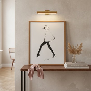Preview: Garance Doré art print poster MY CAPE in slim warm oak frame leaning against softly washed plaster wall on narrow console table with small clear glass vase of dried pampas grass, stack of two coffee-table fashion books with muted spines, slim brass pictur