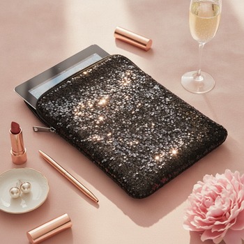 Preview: HOVMAN sequined iPad sleeve with shimmering all-over sequin texture, lying flat slightly angled on pale-pink soft velvet surface with iPad peeking just slightly out of open top, rose-gold lipstick, slim rose-gold pen, flute of champagne, pearl earrings on