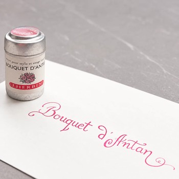 Preview: Kalligrafischer Schriftzug Bouquet d’Antan in Rosenrosa auf weißem Papier vor dunklem Hintergrund