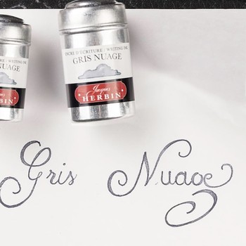 Nahaufnahme der grauen Gris Nuage Kalligrafie neben zwei Jacques Herbin Aluminiumdosen