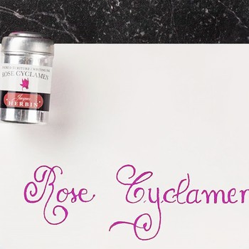 Nahaufnahme der pinkfarbenen Rose Cyclamen Kalligrafie neben Jacques Herbin Aluminiumdose