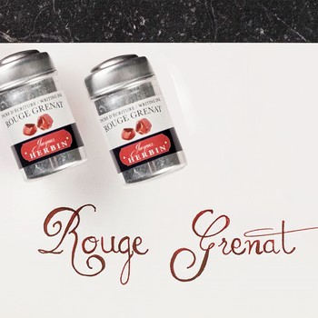 Preview: Zwei Jacques Herbin Rouge Grenat Aluminiumdosen neben kalligrafischem Schriftzug in Granatrot