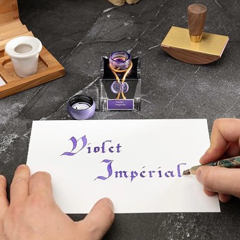 Preview: Kalligrafie mit Jacques Herbin Violet Impérial Tinte auf weißem Papier neben geöffnetem Tintenfass