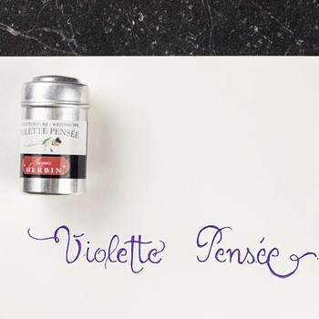 Preview: Jacques Herbin Violette Pensée Aluminiumdose neben violettem Kalligrafie-Schriftzug auf Papier