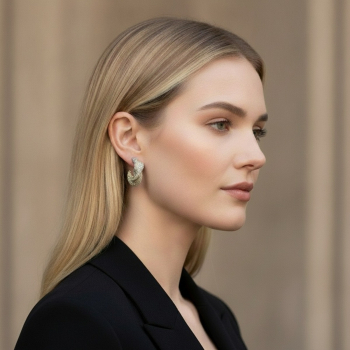 Preview: KMO Creolen SPIRELLI cream on the ear of an elegant blonde woman with shoulder-length natural hair. Sculptural statement half-hoop in a spiral-curl shape, densely set with fine champagne-cream glitter pavé and subtle silver highlights at the top of the po
