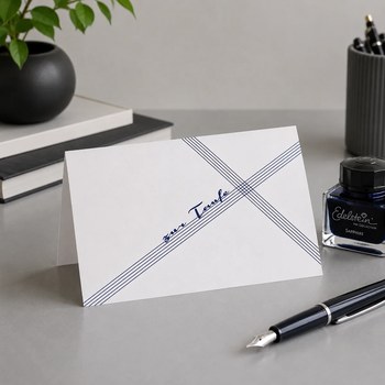 Preview: Trixi Gronau ZUR TAUFE Glueckwunschkarte, B6 Hochformat mit feinen marineblauen diagonalen Linien die sich kreuzen, in der Mitte in fliessender marineblauer Handschrift zur Taufe. Aufgestellt auf weicher cremefarbener Strickdecke mit kleinem Strauss weiss