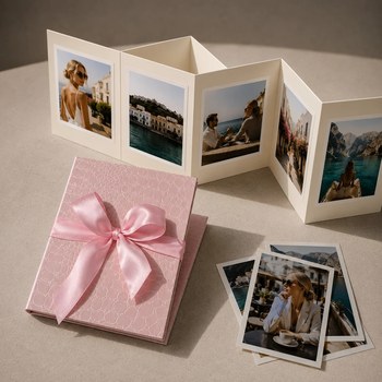 Preview: Trixi Gronau NELLI Fotoleporello Croco rosa, kleines aufgefaltetes Leporello-Album mit fuenf Reisefotos. Daneben das geschlossene Album in rosa Croco-Praegung, verpackt mit zarter rosa Satinschleife. Drei zusaetzliche Polaroid-Fotos. Auf hellem cremefarbe