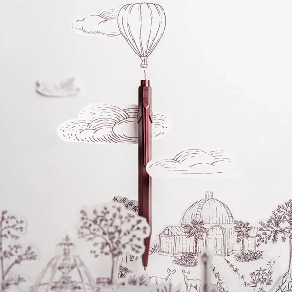 Caran d'Ache 849 Toile de Jouy Burgundy in front of a paper-cut scene from the Geneva illustration