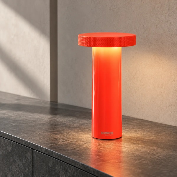 Sompex VOLUME Neon Orange Akku-Tischleuchte auf dunklem Sideboard, Hintergrund KI-Visualisierung