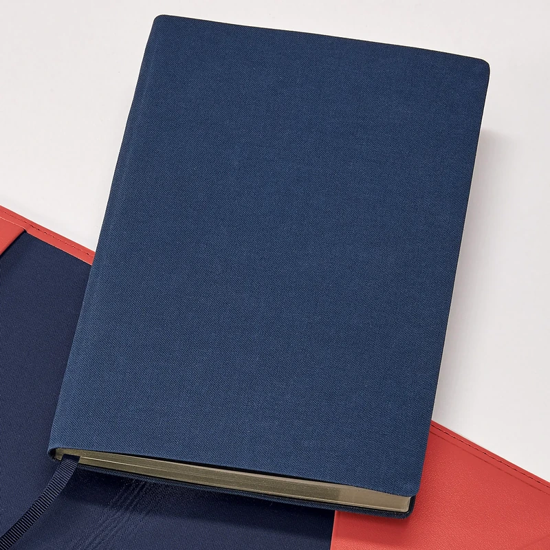 TREULEBEN Journal Refill M dotted in Dunkelblau mit Pale Gold Schnittkante, liegend auf einer roten Hülle