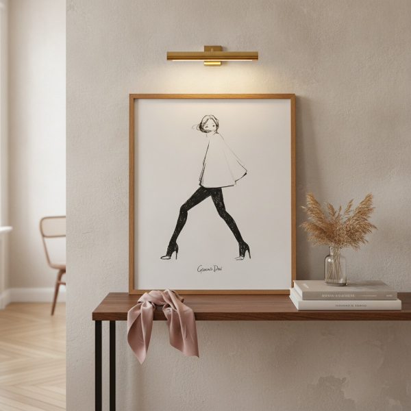 Garance Doré art print poster MY CAPE in slim warm oak frame leaning against softly washed plaster wall on narrow console table with small clear glass vase of dried pampas grass, stack of two coffee-table fashion books with muted spines, slim brass pictur