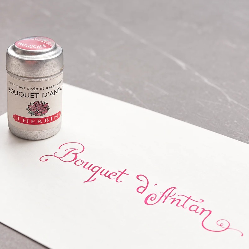 Kalligrafischer Schriftzug Bouquet d’Antan in Rosenrosa auf weißem Papier vor dunklem Hintergrund