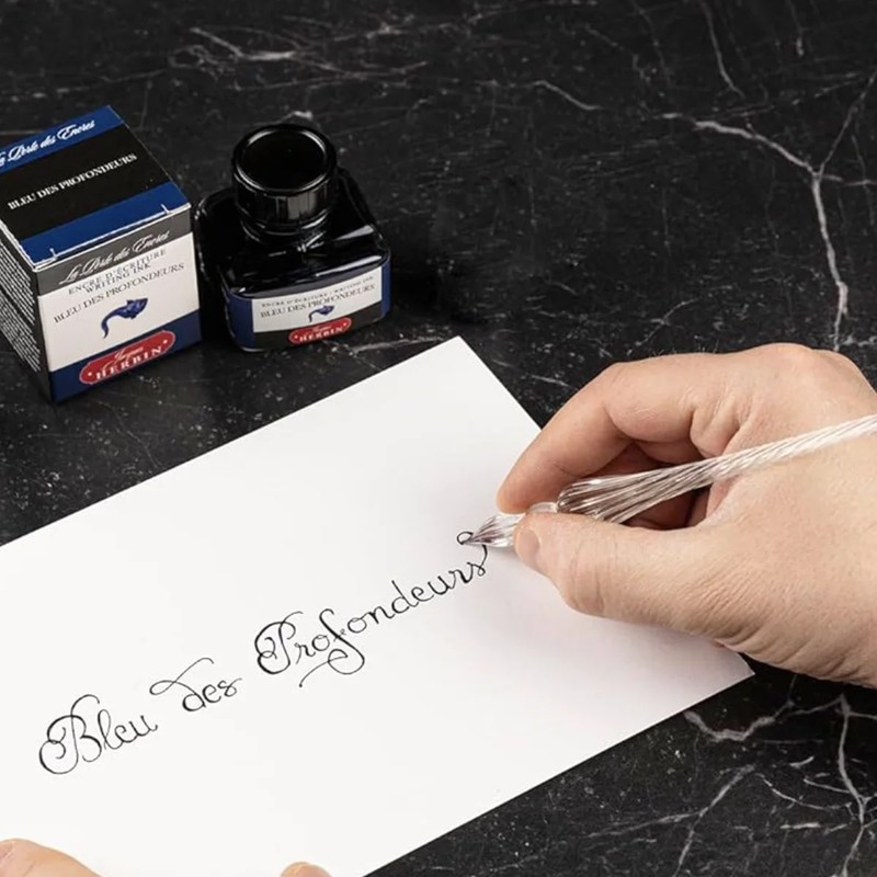 Schriftzug Bleu des Profondeurs auf weißem Papier neben Tintenflakon und Verpackung