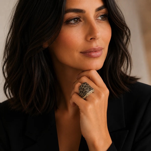 Kmo Ring PATTERN als Statement-Cocktailring mit braun-goldenem Netz-Muster am Finger einer eleganten Brünetten, getragen zu klassischem schwarzem Blazer. Editoriales Portrait, urbane Eleganz. Trixi Gronau Concept Store, Hamburg-Lokstedt.