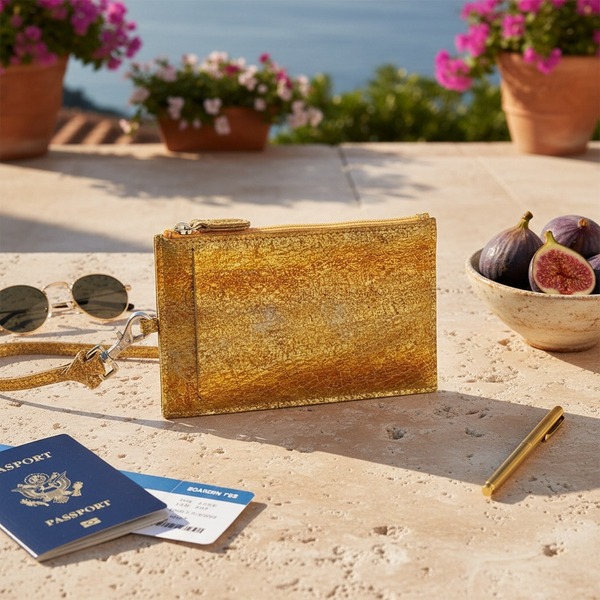 Trixi Gronau RIZZI Brustbeutel gold Schlangenleder-Prägung mit Reissverschluss und Handschlaufe, auf warmem Travertin mit Reisepass, Boardingpass, Vintage-Sonnenbrille gold, Messingstift und frischen Feigen auf eleganter italienischer Riviera-Terrasse